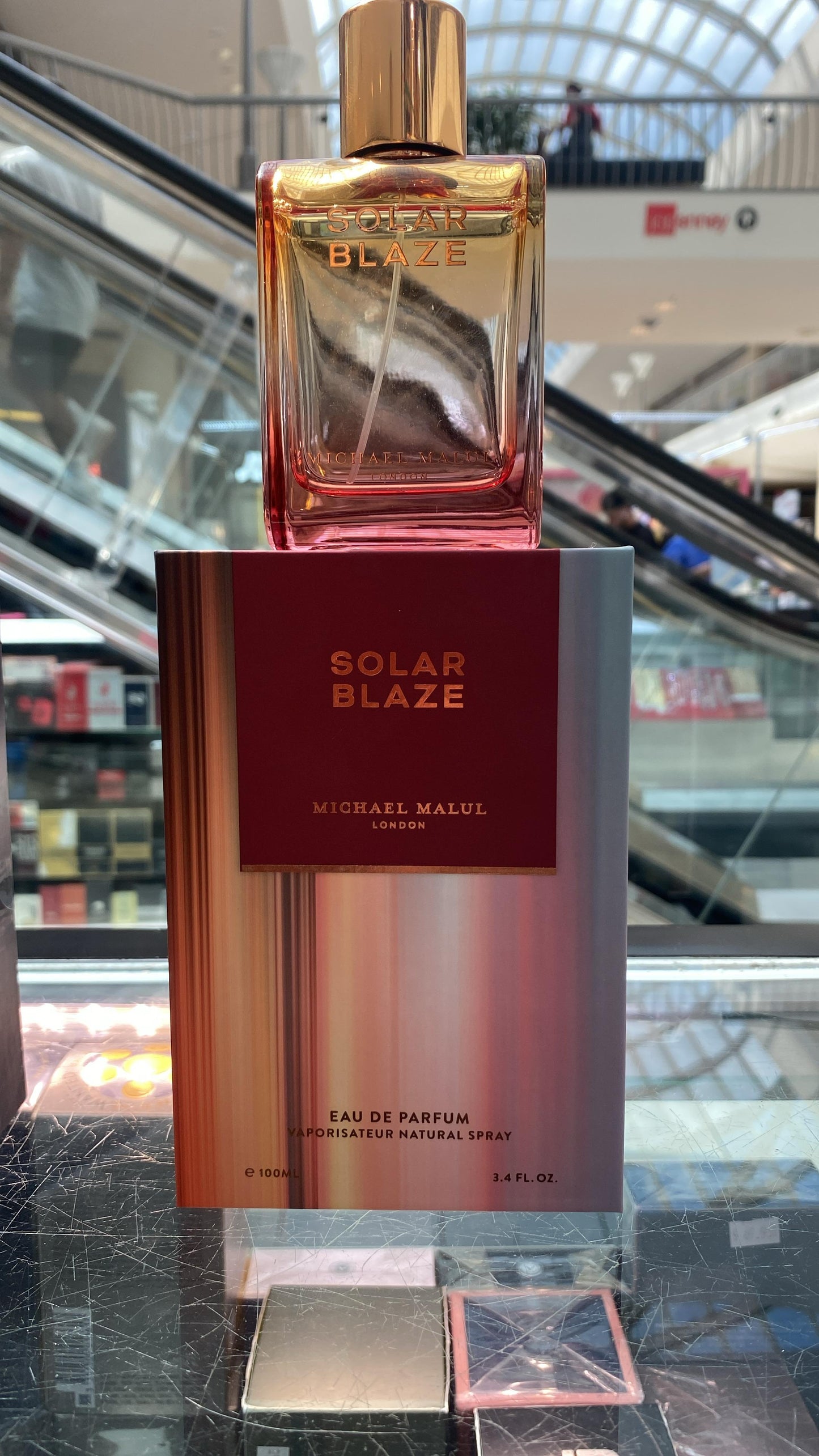 Michael Malul Solar Blaze Eau de Parfum bottle and its outer packaging box, displayed on a glass counter in a shopping mall setting.